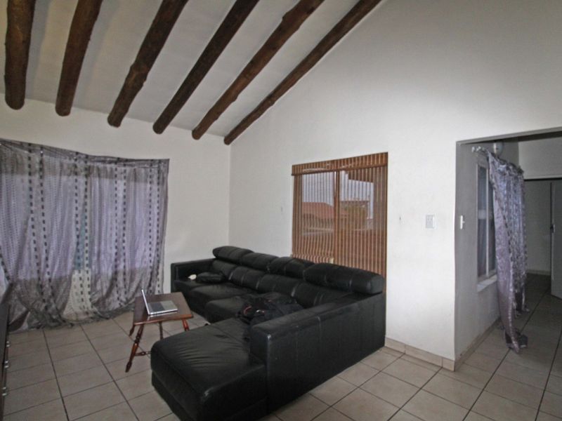 Living room featuring a vaulted ceiling with exposed timber beams and tiled flooring, providing a spacious and rustic atmosphere.