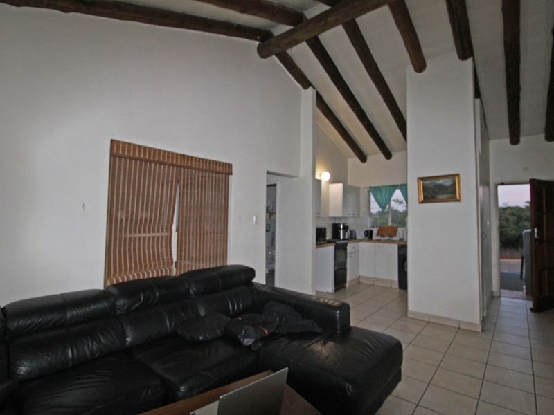 Open plan living area featuring vaulted ceilings with exposed timber beams and tiled flooring, seamlessly connecting to a functional kitchen space.