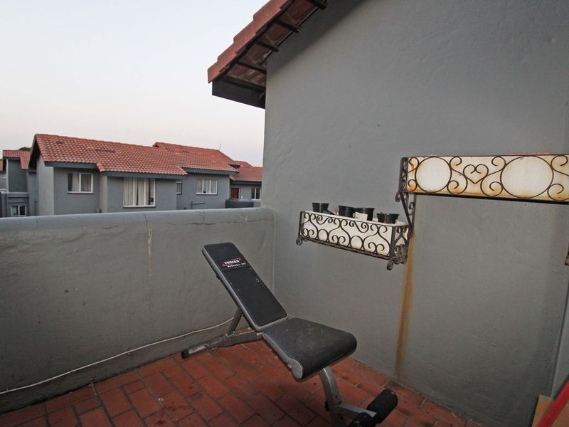 A compact balcony featuring tiled flooring and decorative wrought iron wall planters, offering an outdoor space with views of the surrounding complex.