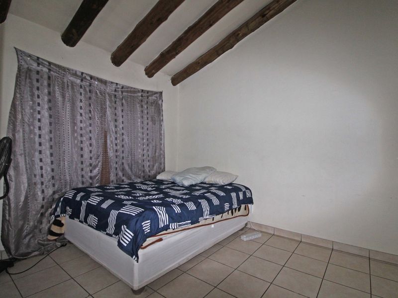 A bedroom featuring exposed timber ceiling beams and tiled flooring, offering a rustic aesthetic with potential for modern updates.