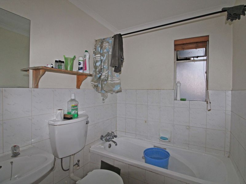 A functional bathroom featuring a bathtub, pedestal basin, and toilet with tiled splashbacks and a window for natural light.