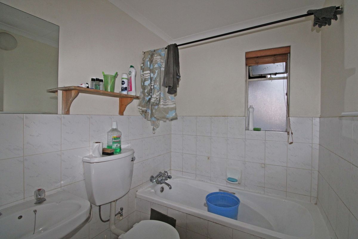A functional bathroom featuring a bathtub, pedestal basin, and toilet with tiled splashbacks and a window for natural light.