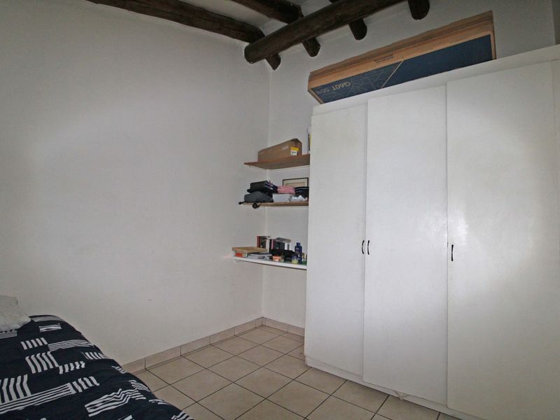 A bedroom featuring tiled flooring, exposed timber ceiling beams, and a built-in wardrobe with additional wall-mounted shelving.