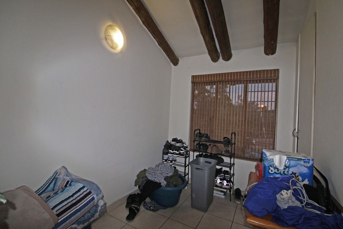 A bedroom featuring exposed timber ceiling beams, tiled flooring, and a window with fitted blinds, offering a functional space with character.