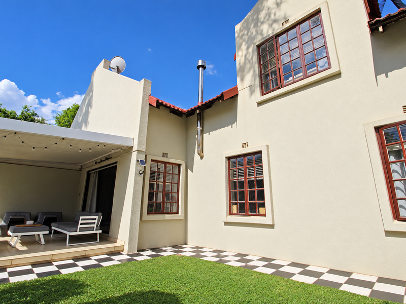 Rear view of the townhouse featuring a covered patio area, checkered tiled flooring, and a well-maintained plastered facade with timber-framed windows.
