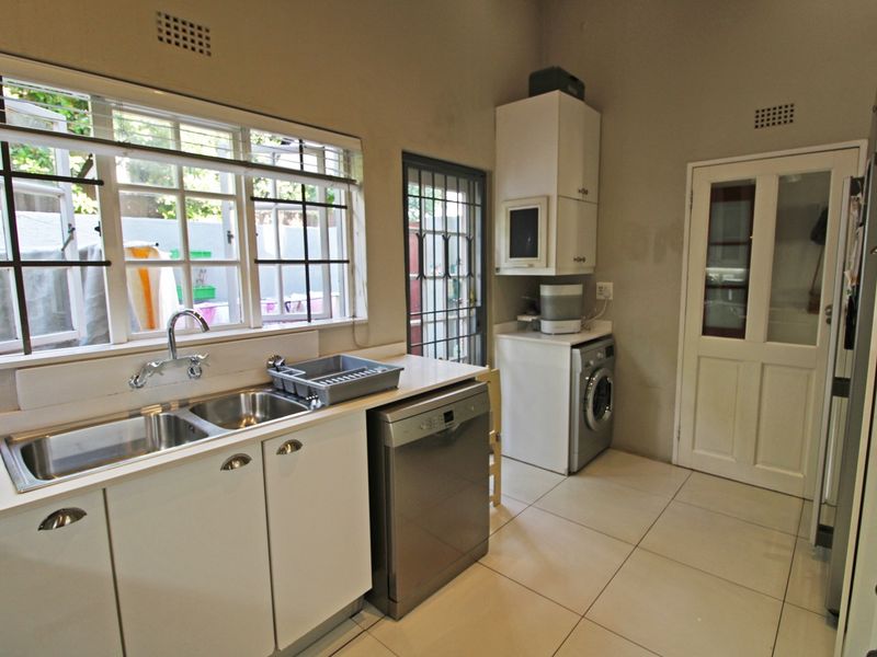 Functional kitchen featuring tiled flooring, double stainless steel sink, built-in cabinetry, and direct access to the exterior via a security gate.