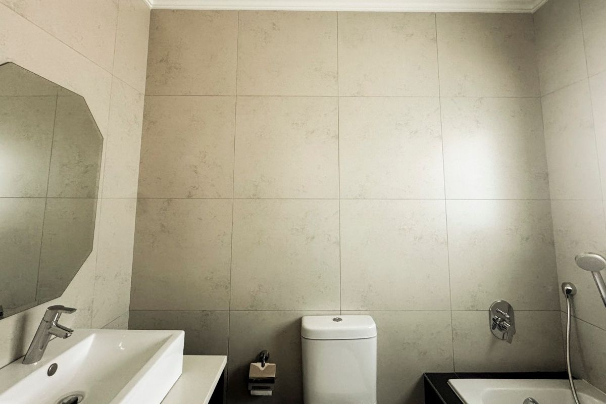 A modern, neutral-toned bathroom featuring a wall-mounted basin, a sleek toilet, and a bathtub with a handheld shower fixture.