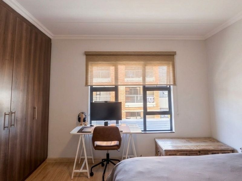 A well-maintained bedroom featuring built-in cupboards, laminate flooring, and a large window with a roller blind, providing ample natural light.