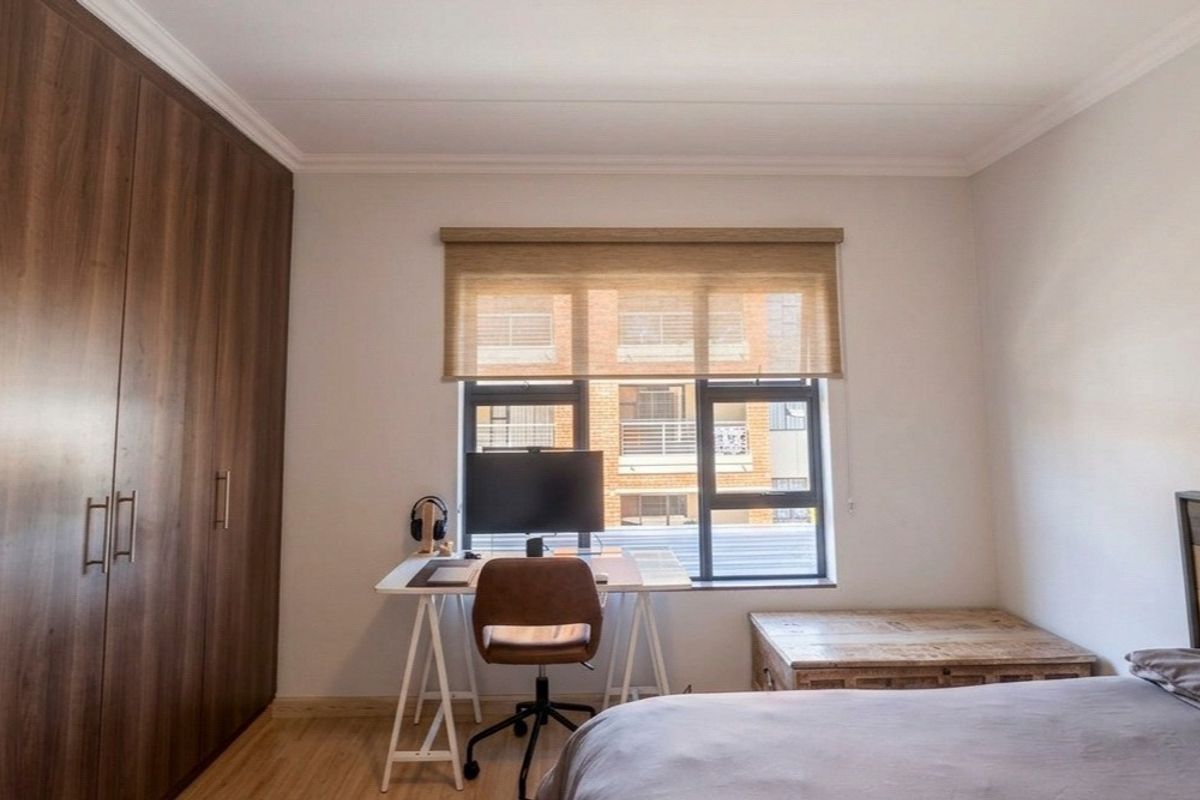 A well-maintained bedroom featuring built-in cupboards, laminate flooring, and a large window with a roller blind, providing ample natural light.