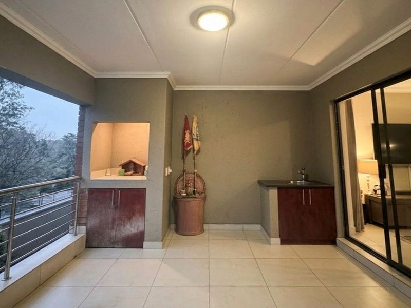 Covered balcony featuring a built-in braai, kitchenette with sink, tiled flooring, and sliding door access to the interior living space.