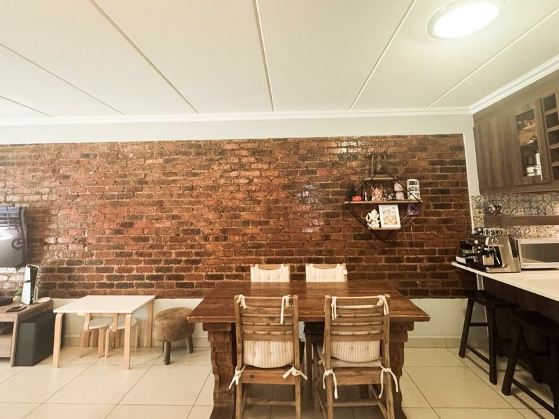 Open plan living and dining area featuring a prominent exposed brick feature wall, tiled flooring, and a modern kitchen with stone countertops.