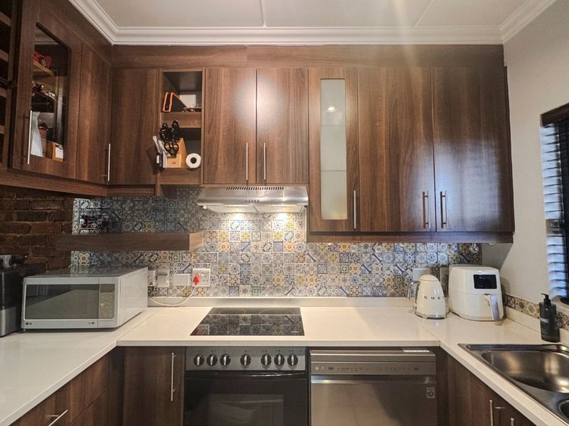 A well-maintained kitchen featuring dark wood cabinetry, stone countertops, a patterned tile backsplash, and integrated appliances including an oven, hob, and dishwasher.