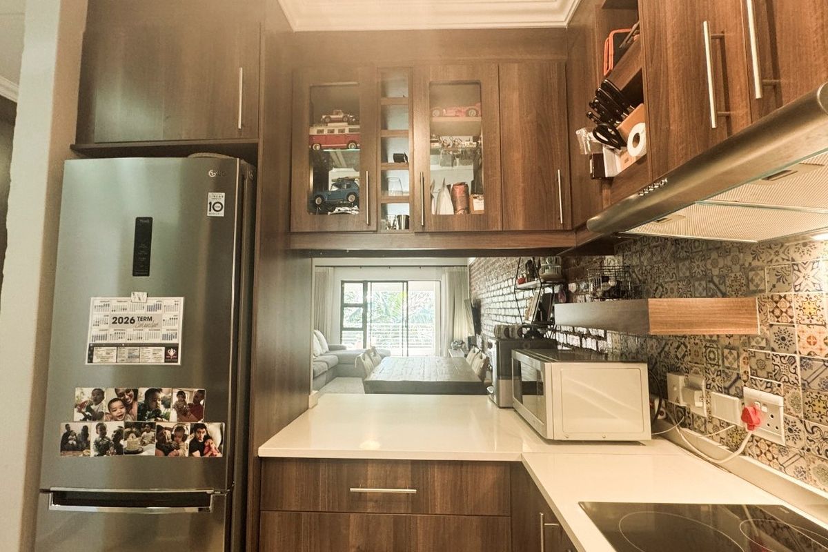 Modern kitchen featuring wood-finish cabinetry, quartz countertops, a decorative tile backsplash, and integrated appliances, with a view through to the living area.