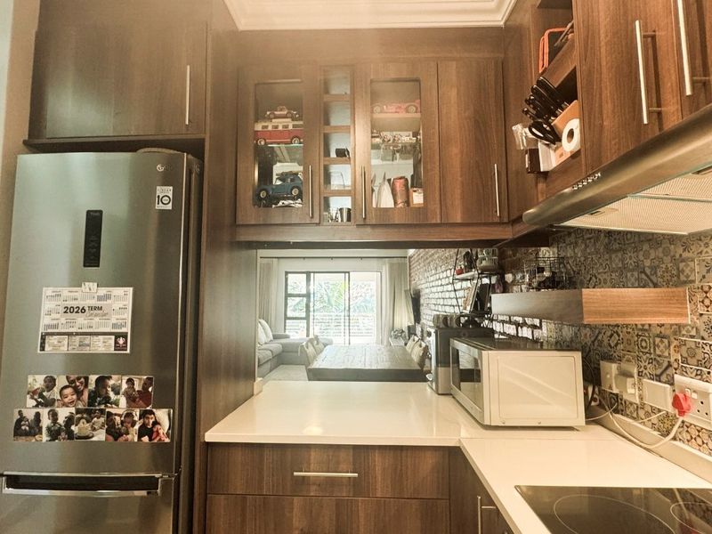 Modern kitchen featuring wood-finish cabinetry, quartz countertops, a decorative tile backsplash, and integrated appliances, with a view through to the living area.