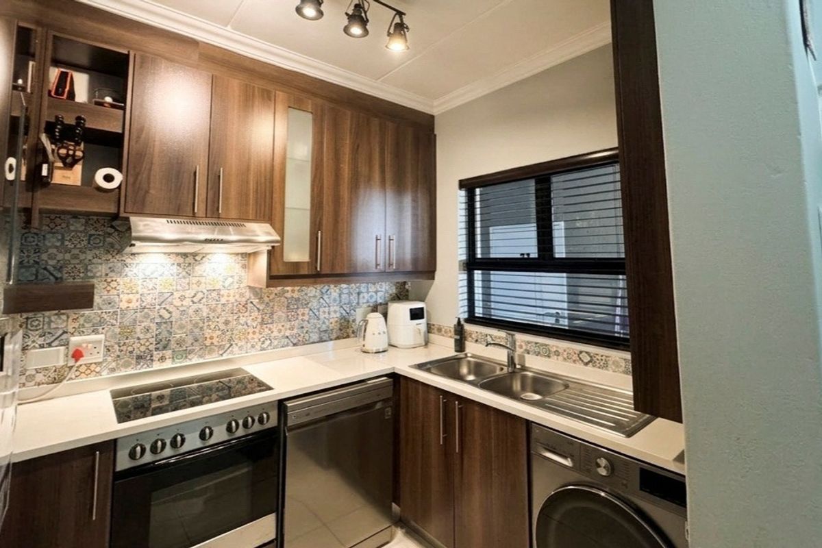 Modern kitchen featuring dark wood cabinetry, quartz countertops, a decorative tiled backsplash, integrated appliances, and functional track lighting.