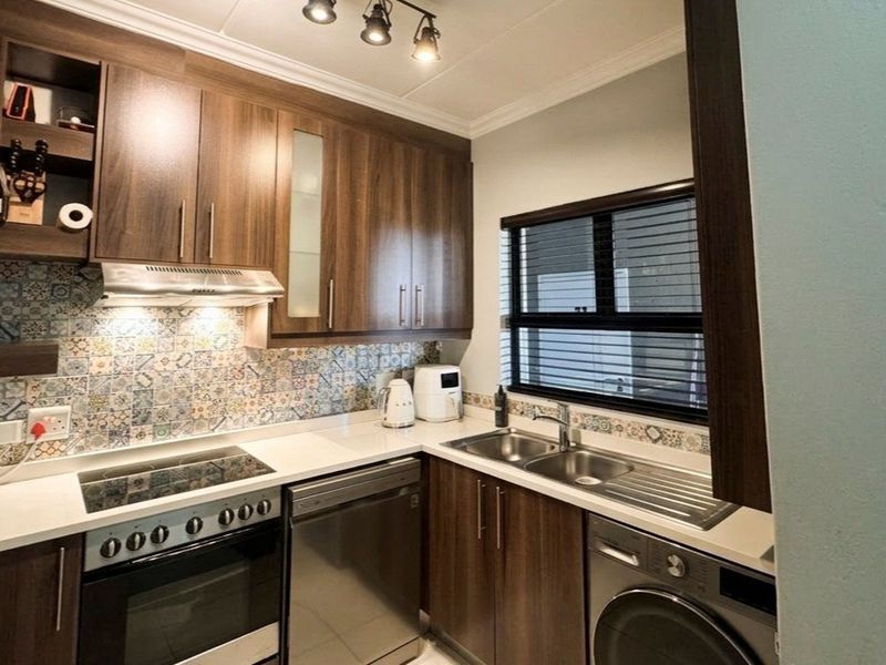Modern kitchen featuring dark wood cabinetry, quartz countertops, a decorative tiled backsplash, integrated appliances, and functional track lighting.
