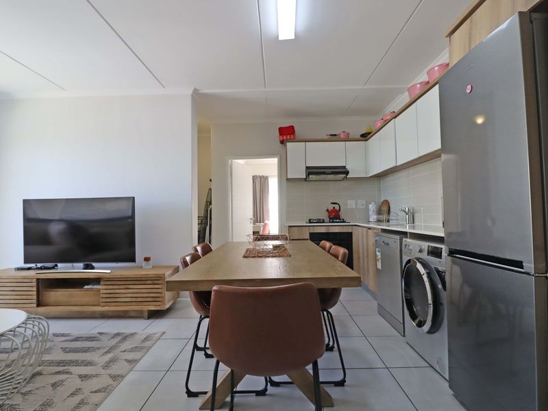 An open-plan living and kitchen area featuring modern cabinetry, tiled flooring, and integrated kitchen appliances in a well-maintained apartment setting.