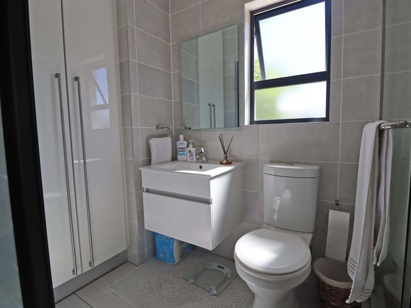 Modern bathroom featuring a wall-mounted vanity, ceramic toilet, and neutral tiled finishes with a functional top-hung window for natural light.