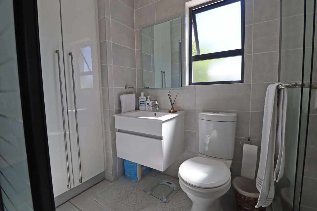 Modern bathroom featuring a wall-mounted vanity, ceramic toilet, and neutral tiled finishes with a functional top-hung window for natural light.