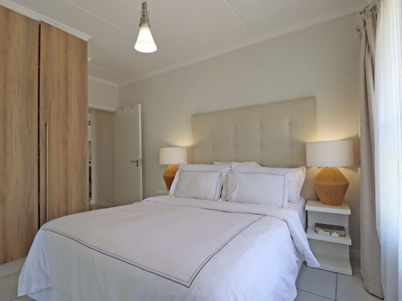 A well-maintained bedroom featuring neutral tones, tiled flooring, and a large built-in wardrobe with wood-grain finish.