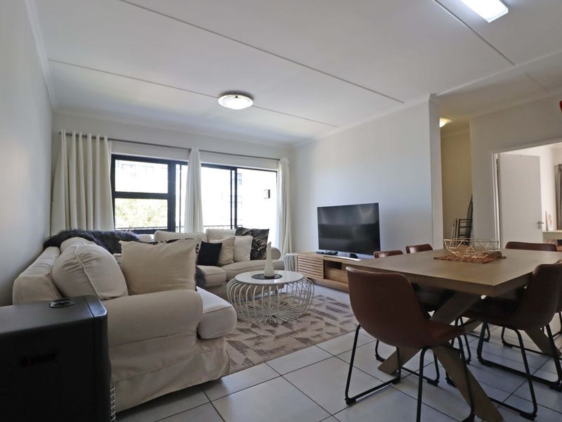 A bright open-plan living and dining area featuring tiled flooring, neutral walls, and large sliding glass doors that provide ample natural light.