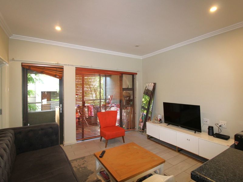 A well-lit living room featuring tiled flooring, crown molding, and a sliding glass door that opens to a balcony with venetian blinds.