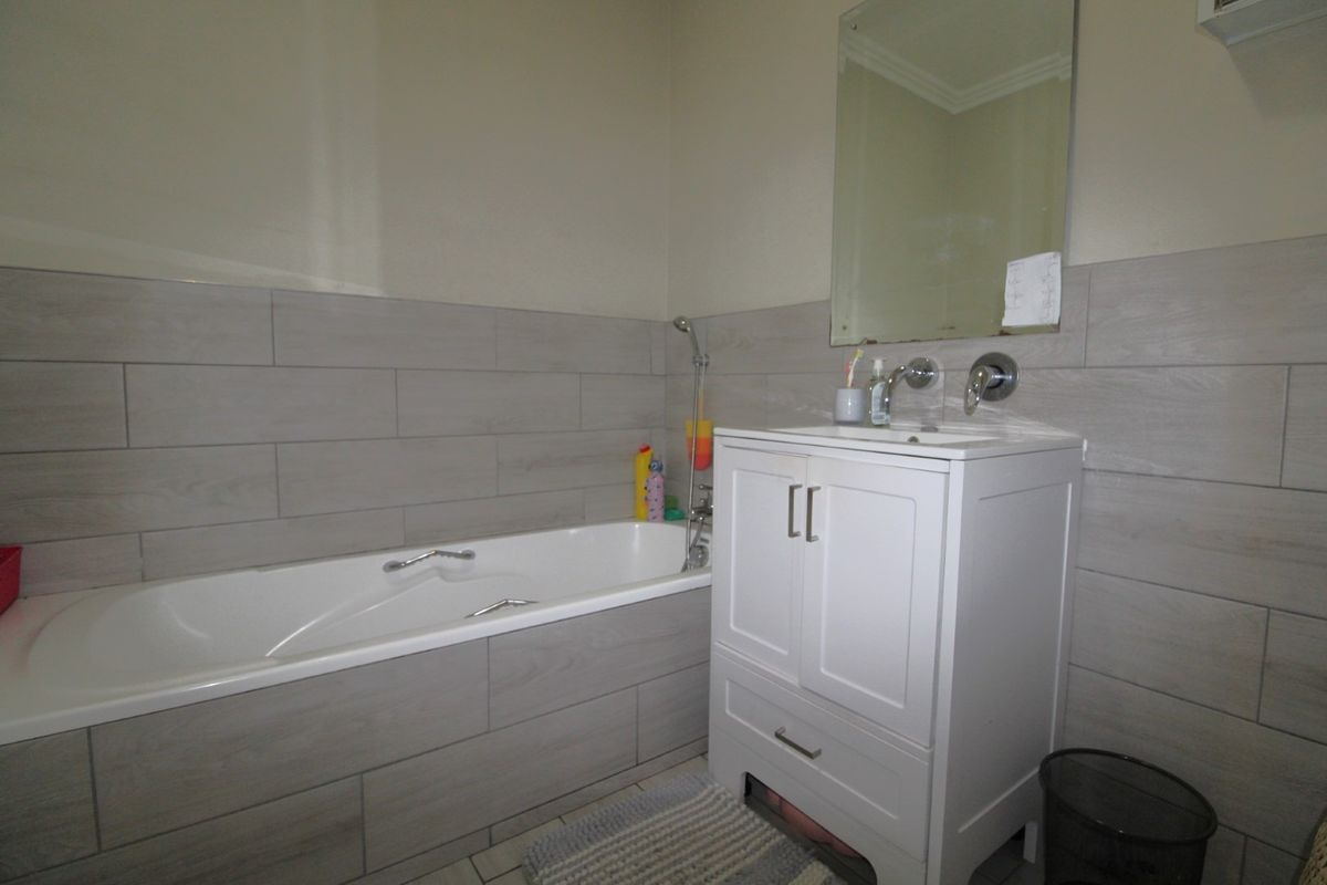 A modern bathroom featuring a built-in bathtub, a white vanity cabinet with a wall-mounted faucet, and neutral wood-look wall tiling.