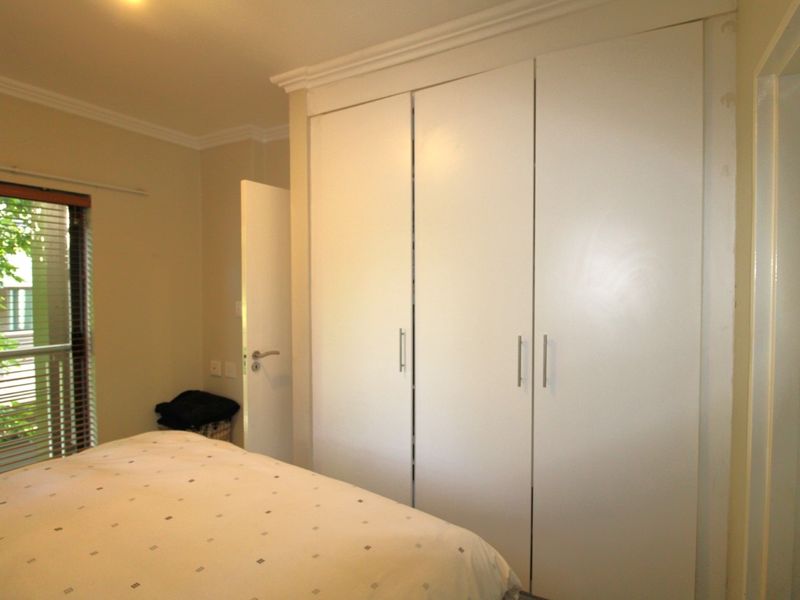 A well-maintained bedroom featuring ample built-in cupboard storage, crown molding, and natural light through a window with venetian blinds.
