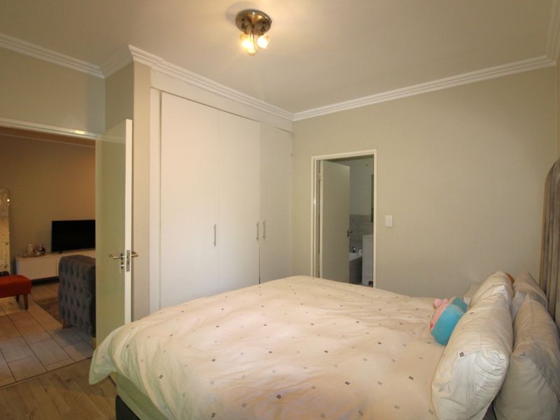 A well-maintained bedroom featuring built-in cupboards, crown molding, and laminate flooring, with direct access to an en-suite bathroom and adjacent living area.