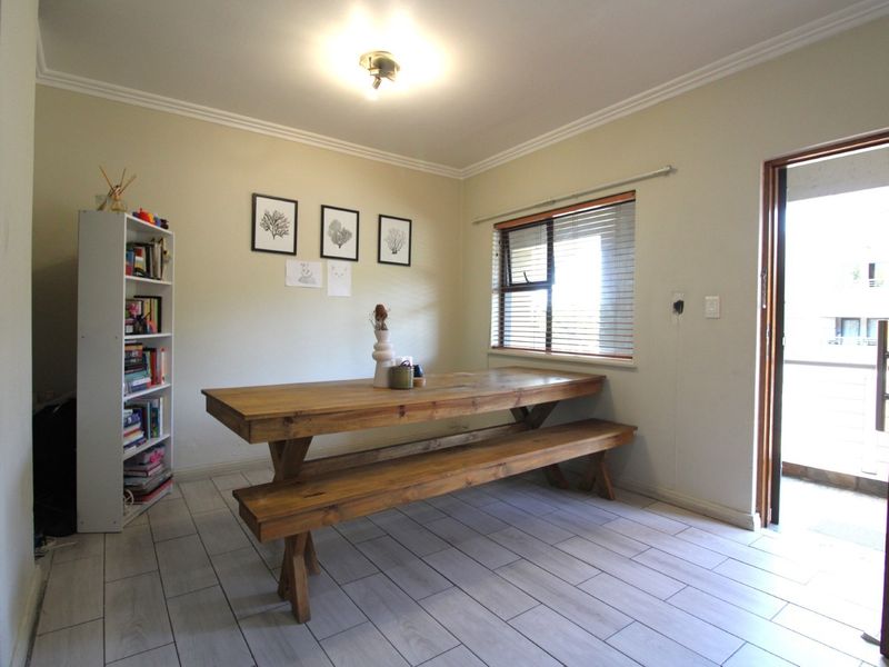 A functional dining area featuring light-toned tiled flooring, neutral walls, and natural light through a window with fitted venetian blinds.