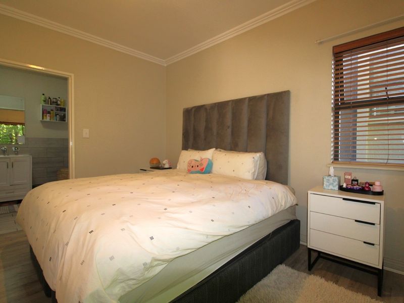 A well-maintained bedroom featuring neutral wall tones, crown molding, and laminate flooring, with an adjoining bathroom visible through the doorway.