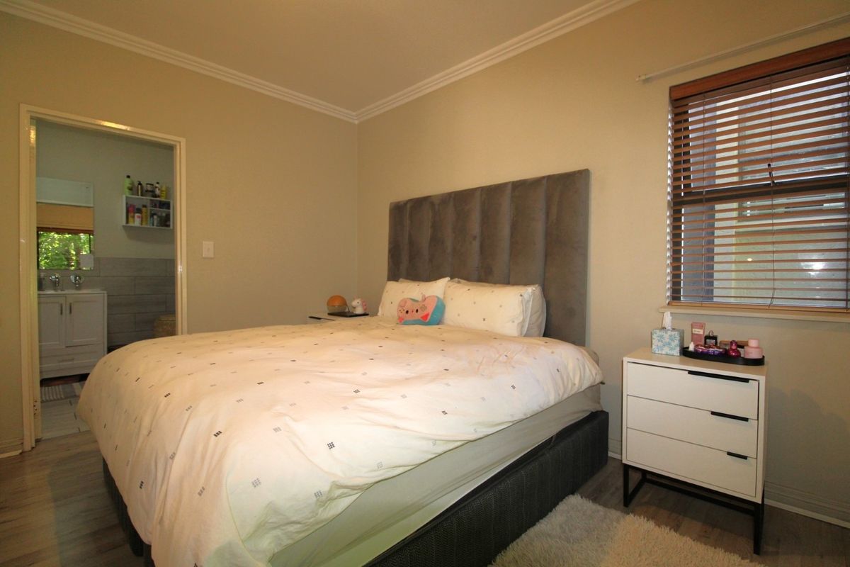 A well-maintained bedroom featuring neutral wall tones, crown molding, and laminate flooring, with an adjoining bathroom visible through the doorway.
