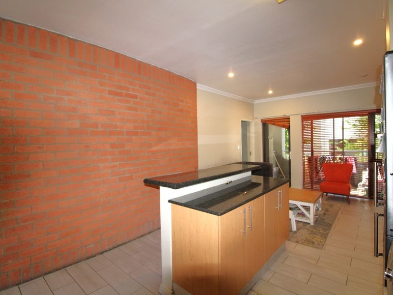 Open plan living area featuring an exposed brick feature wall, kitchen island with granite countertop, tiled flooring, and direct access to an outdoor patio.