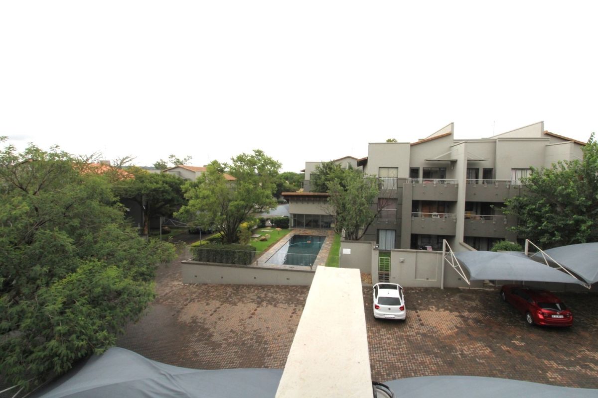 An elevated view of the apartment complex grounds, featuring a swimming pool, paved parking area with shade cloth carports, and established garden landscaping.