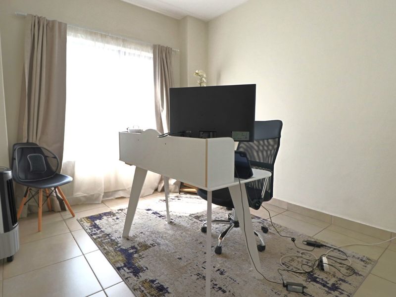 A bright home office space featuring neutral wall finishes and tiled flooring, illuminated by natural light through a large window.