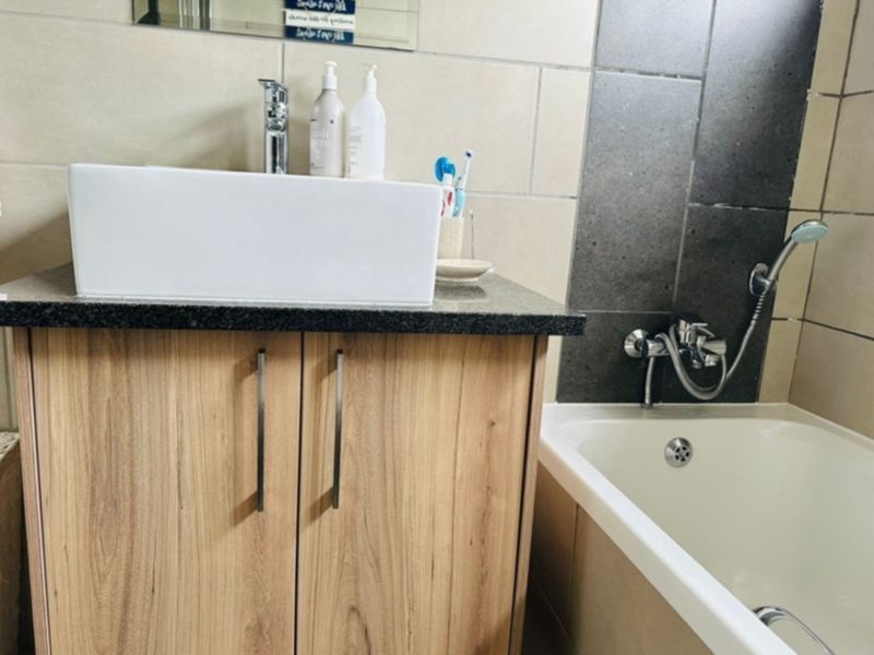 A modern bathroom featuring a vessel sink on a granite vanity countertop, wooden cabinetry, and a bathtub with a handheld shower mixer.