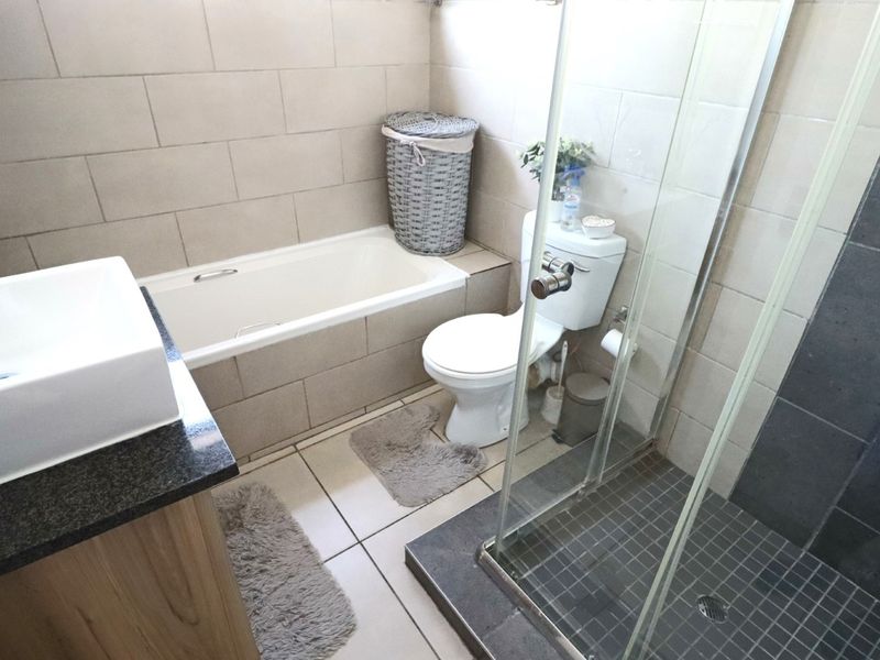 A functional bathroom featuring a built-in bathtub, separate glass-enclosed shower, toilet, and a modern vanity with a countertop basin.