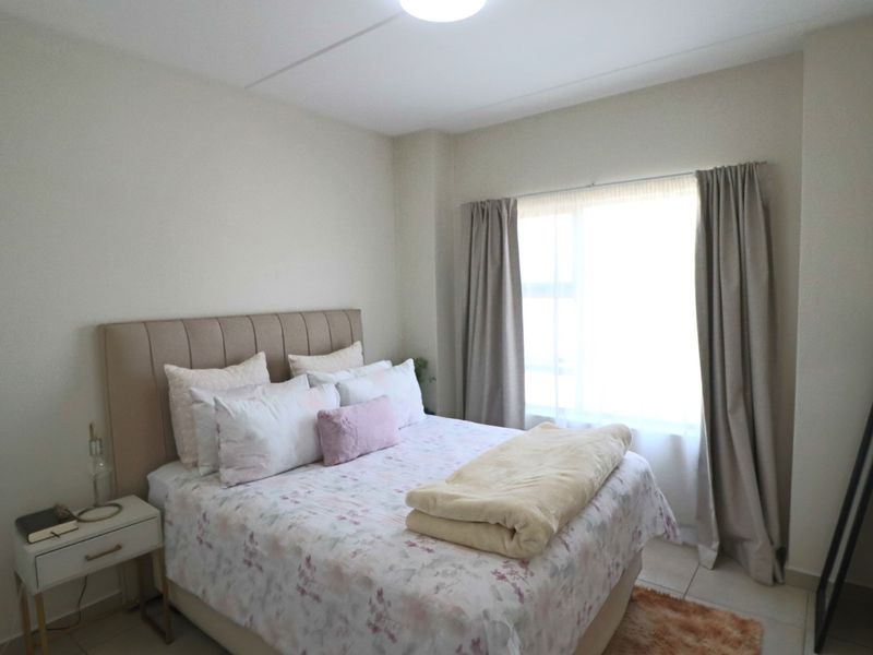 A well-lit bedroom featuring neutral wall tones, tiled flooring, and large windows with installed curtain tracks.