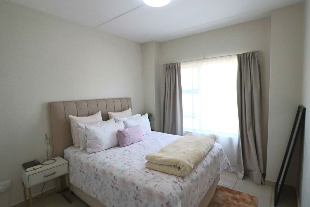 A well-lit bedroom featuring neutral wall tones, tiled flooring, and large windows with installed curtain tracks.