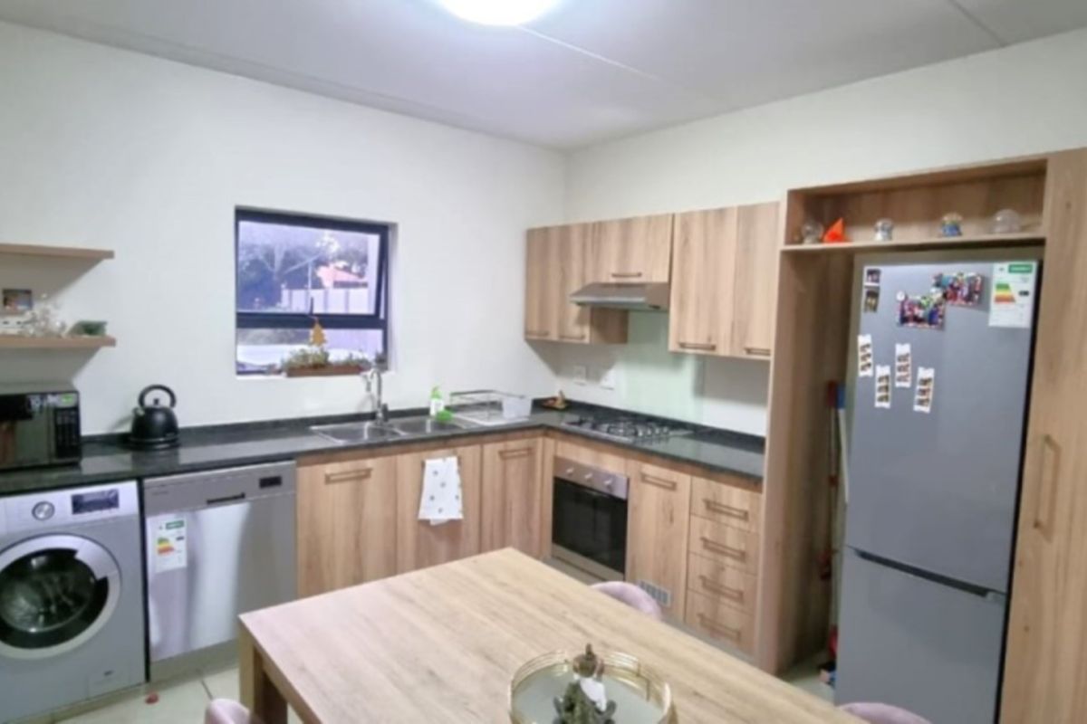 A modern kitchen featuring light wood-finish cabinetry, dark countertops, built-in oven with gas hob, and dedicated spaces for laundry and dishwasher appliances.