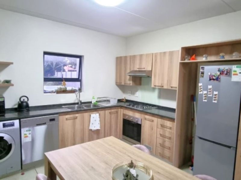A modern kitchen featuring light wood-finish cabinetry, dark countertops, built-in oven with gas hob, and dedicated spaces for laundry and dishwasher appliances.