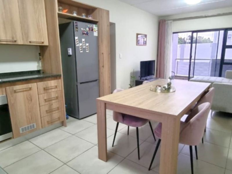 An open-plan living and kitchen area featuring modern wood-finish cabinetry, granite countertops, integrated appliances, and direct access to a balcony through sliding doors.