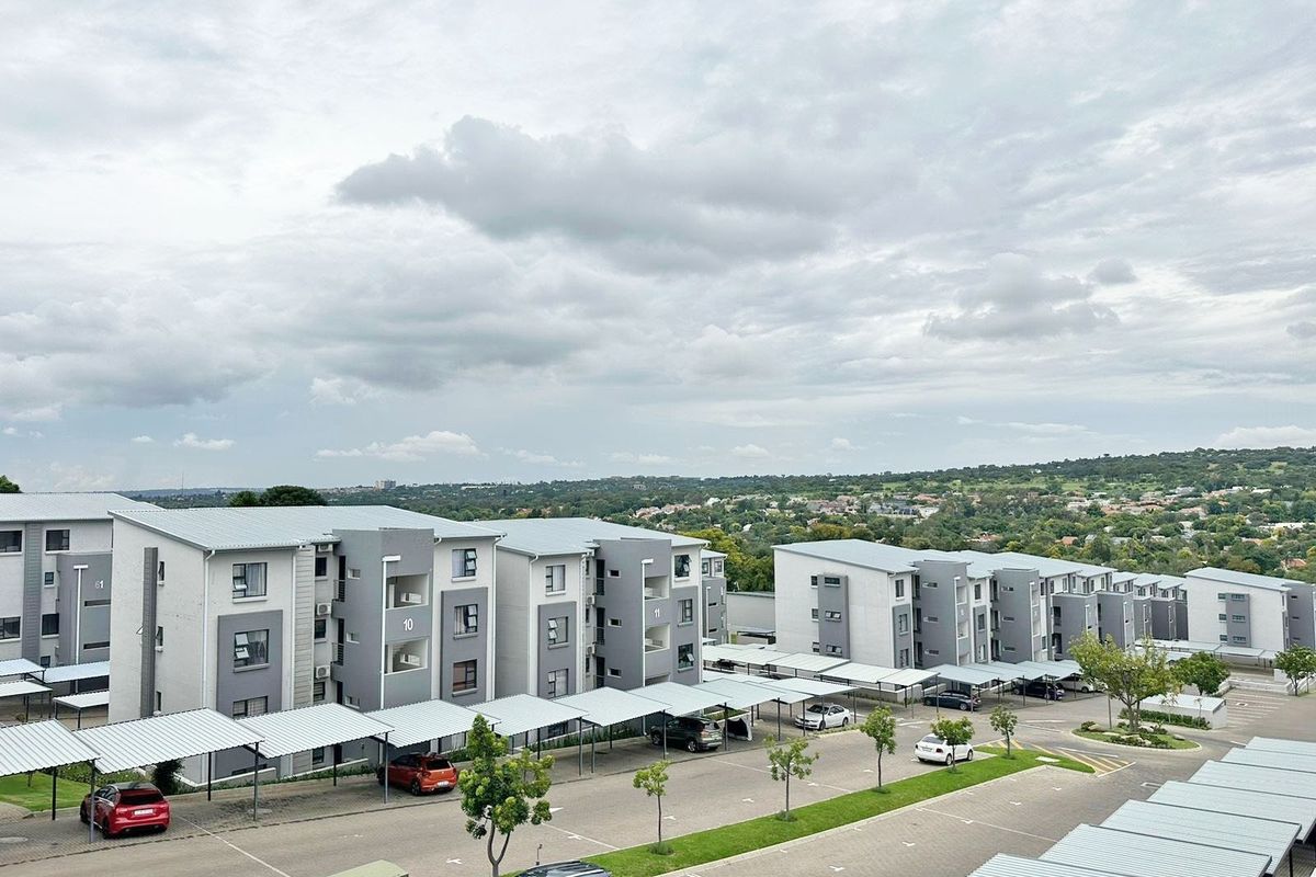 An aerial view of a modern apartment complex featuring multiple residential blocks, covered parking bays, and landscaped grounds under a cloudy sky.