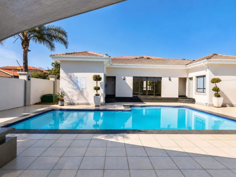 A well-maintained outdoor pool area featuring a clear swimming pool, tiled decking, and a shade sail, providing a clean and inviting space.
