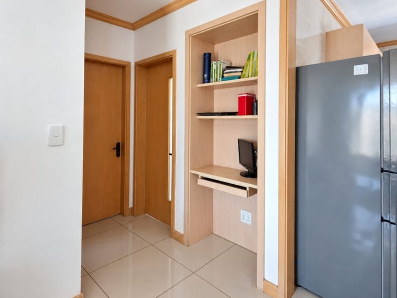 A well-maintained hallway featuring tiled flooring, timber door frames, and a convenient built-in study nook with integrated shelving.