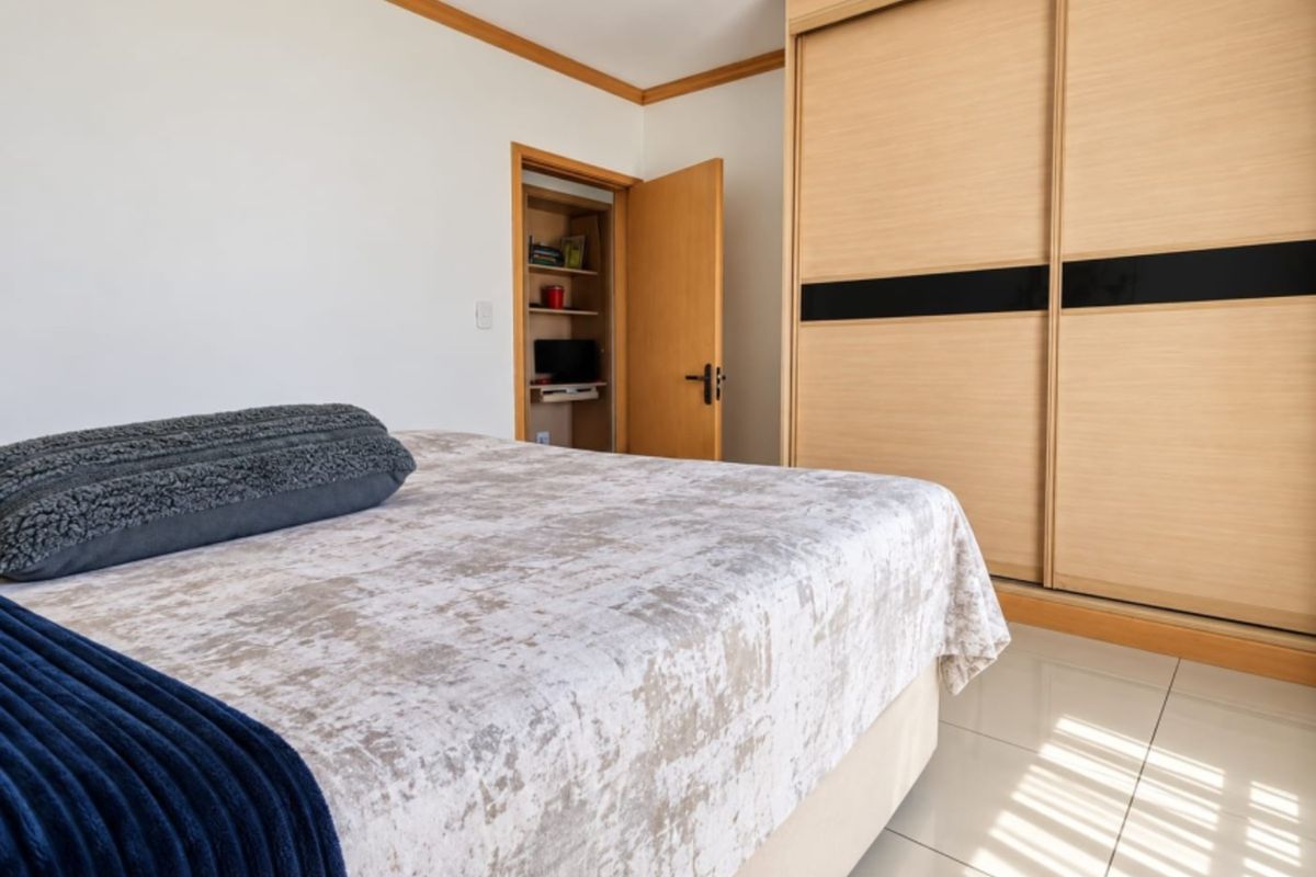 A well-maintained bedroom featuring light-toned built-in sliding wardrobes, tiled flooring, and a convenient integrated storage closet.