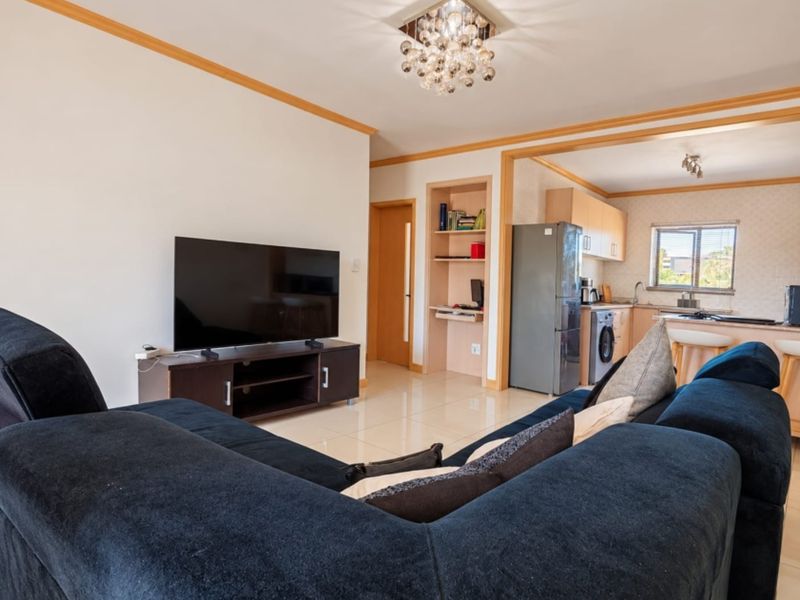 Open plan living area featuring tiled floors, built-in shelving, and an adjoining kitchen with cabinetry and integrated appliances.