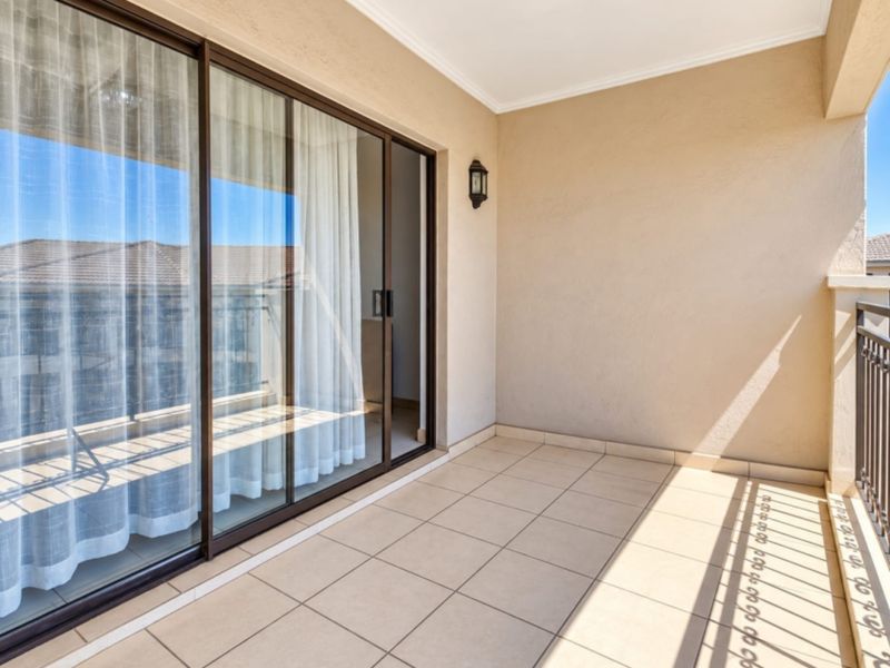 A clean, covered balcony featuring tiled flooring, a metal balustrade, and large sliding glass doors providing access to the interior living space.