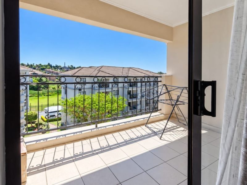 A clean, tiled balcony featuring a decorative wrought iron balustrade and pleasant views of the surrounding residential complex.