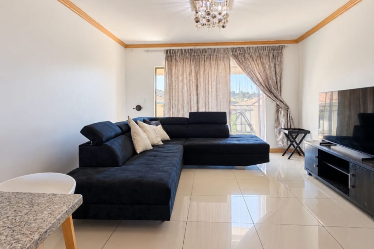 A bright and spacious living room featuring polished porcelain floor tiles, crown molding, and a sliding glass door leading to an outdoor area.